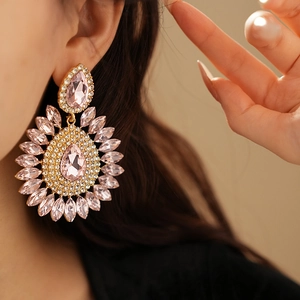 Macro shot of gold teardrop earrings with pink and clear crystals on a model