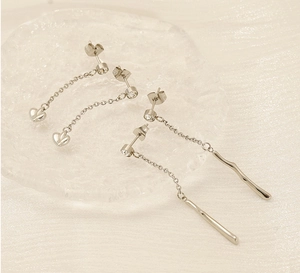 Detail of silver tassel earrings with heart and bar pendants on ice cube prop