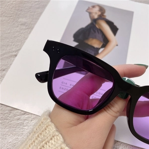 Detail of square black frame sunglasses with purple lenses over a fashion magazine