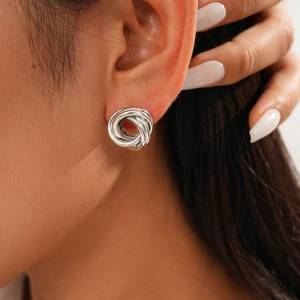 Close-up detail of silver geometric layered knot stud earrings on female ear