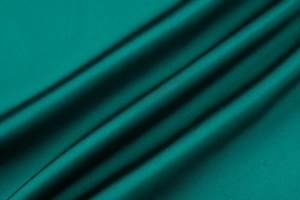 Vue macro du tissu en satin vert émeraude montrant la texture soyeuse et le drapé lisse