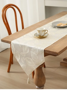 Detail of cream jacquard table runner with leaf pattern and tassel fringe decoration