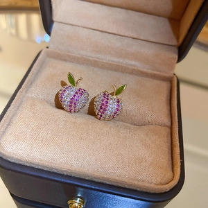 Macro shot of gold apple stud earrings with pink and white cubic zirconia on a jewelry box