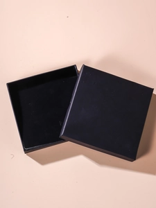 Top view of a square black cardboard gift box with lid for jewelry on a beige surface