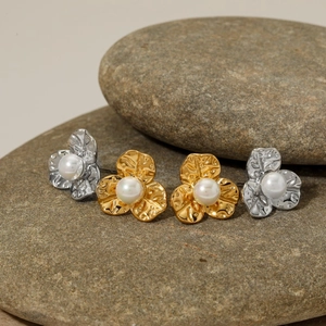 Detail of flower pearl earrings in gold and silver finish on natural pebble stones