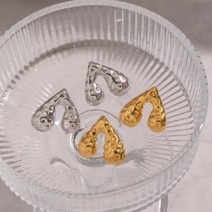 Detailaufnahme goldener und silberner Herzohrringe mit Hammerschlagoptik in Glasschale
