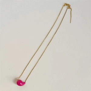 Macro shot of minimalist gold necklace with a glossy pink teardrop-shaped pendant charm