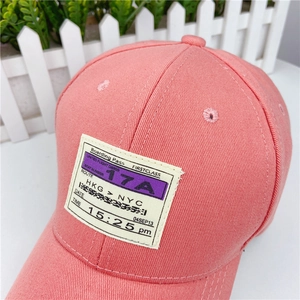Detail of coral pink cotton baseball cap featuring a boarding pass theme woven patch