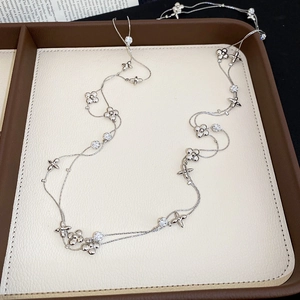 Detail of silver long sweater necklace featuring flower, star, and zircon elements