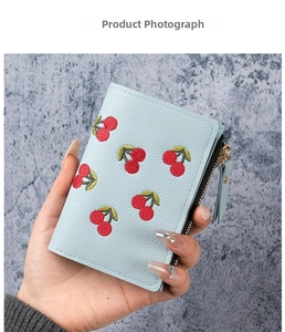 Close-up of light blue wallet with red cherry embroidery and litchi grain texture