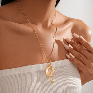 Detailed view of irregular fluid gold pendant and spherical charm necklace on model