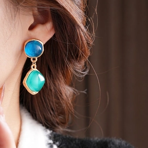 Vintage gold earrings with blue round and green rhombic resin stones on a model