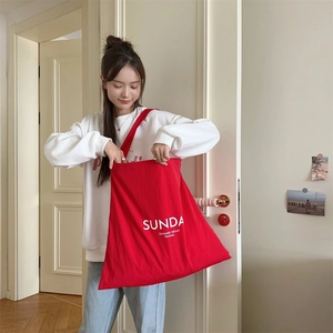 Detail of red canvas tote bag with white lettering worn over the shoulder for commute