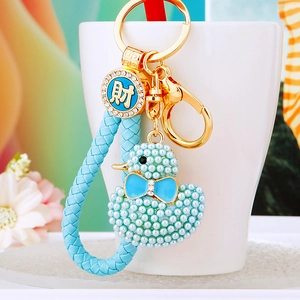 Detail of blue faux pearl duck keychain with woven rope and gold lucky charm tag