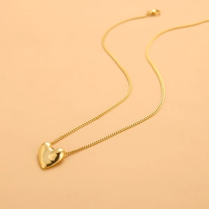 Macro detail of a minimalist gold heart pendant necklace with mirror polished finish