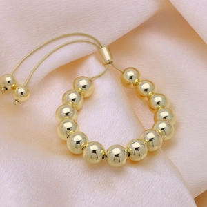 Adjustable 18k gold plated round bead bracelet with pull-string closure on silk background
