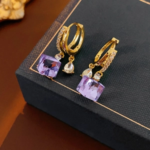 Detail of gold earrings with square purple gems and teardrop stones on a black box