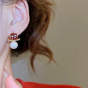 Detailed close-up of 18K gold plated pearl earrings with red enamel dice and zircons