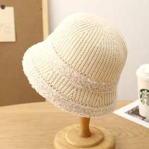 Minimalist cream knit bucket hat with plush trim displayed on a wooden stand