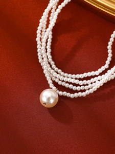 Detail of multilayer white pearl necklace with large round pendant on red fabric