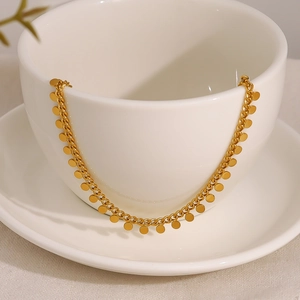 Elegant gold necklace with small round disk pendants draped on a white ceramic cup