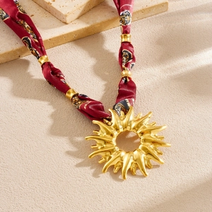 Close-up of golden sunburst pendant with vintage red floral printed silk ribbon strap