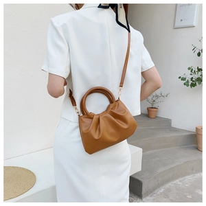 Detail of caramel cloud bag featuring a round handle and pleated texture in a minimalist setting