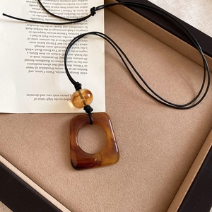 Detail of square amber resin leopard print pendant necklace with black cord on beige box