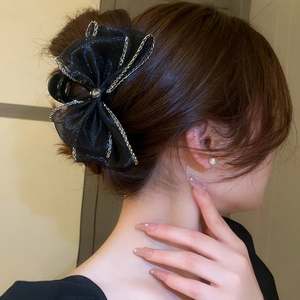 Détail d'une pince à cheveux à nœud en résille noire avec chaîne argentée sur modèle
