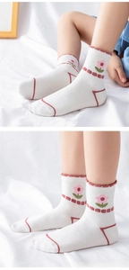 Detail of white cotton baby socks with pink flower patterns and red striped trim