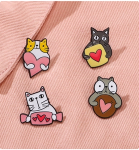 Close-up of four cute metal cat brooches with hearts on pink twill fabric background