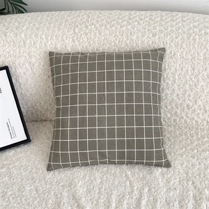Detail of dark green grid cotton linen pillowcase on a soft white fleece sofa