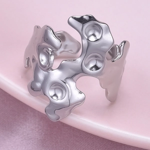 Close-up of irregular liquid metal ring in silver finish on pink silk background