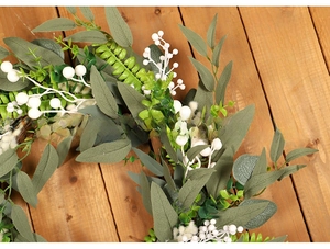 Detail view of artificial white berry and eucalyptus wreath on dark wood background