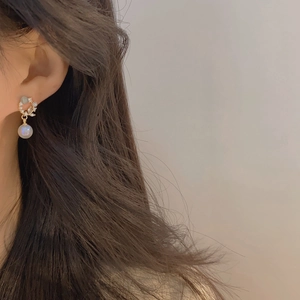 Close-up of French luxury cat-eye stone earrings with pearls and zircon on model's ear