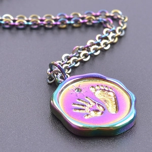 Macro detail of rainbow stainless steel pendant with handprint, footprint and crystal