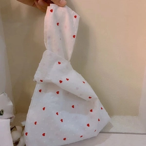 Detail of white knot wrist bag with red heart pattern and textured polka dot fabric
