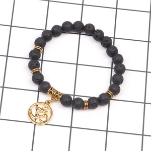 Dettaglio di perle in pietra lavica nera con ciondolo Om dorato su bracciale elastico