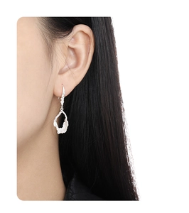 Irregular hollow silver earring with textured surface on a model's ear detail
