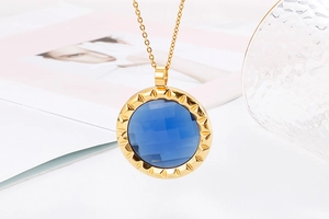 Detail of a round blue crystal pendant with golden jagged edge and metal chain
