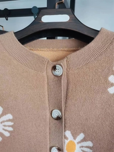 Close-up of floral daisy embroidery and marble texture buttons on camel knit cardigan