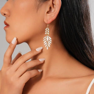 Close-up of elegant gold leaf-shaped earrings with white rhinestones on a female model