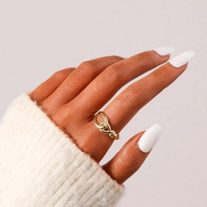 Detail of a gold-plated twisted heart ring worn with a white knit sweater