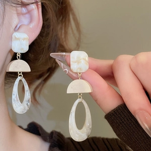 Detail of a minimalist earring made of marble resin and wood held by a hand