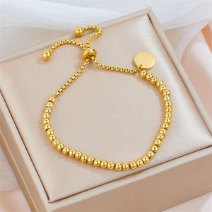 Bracelet ajustable en perles dorées avec pendentif rond sur boîte à bijoux beige