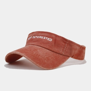 Macro detail of 'NOT INTERESTED' white embroidery on washed rust red sun visor hat