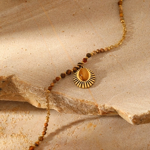 Detail of bohemian gold sun pendant with tiger eye stone on a beaded necklace
