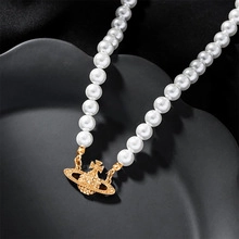 Macro shot of white pearl necklace with gold orb pendant on black silk background
