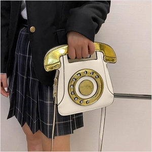 Close-up of white telephone cross-body bag with golden handset handle and dial decoration