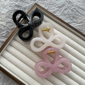 Three jelly-colored clover-shaped hair claws in black, white, and pink in a velvet tray